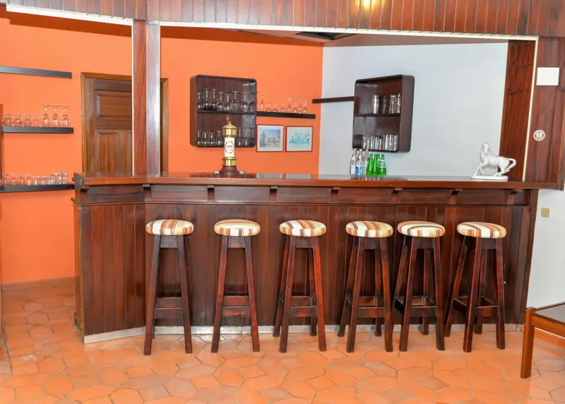 Un comptoir de bar en bois avec des tabourets est présenté dans une pièce aux murs orange.