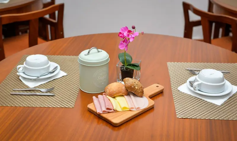 Une table en bois est dressée pour le petit-déjeuner avec de la charcuterie, du pain et des couverts.