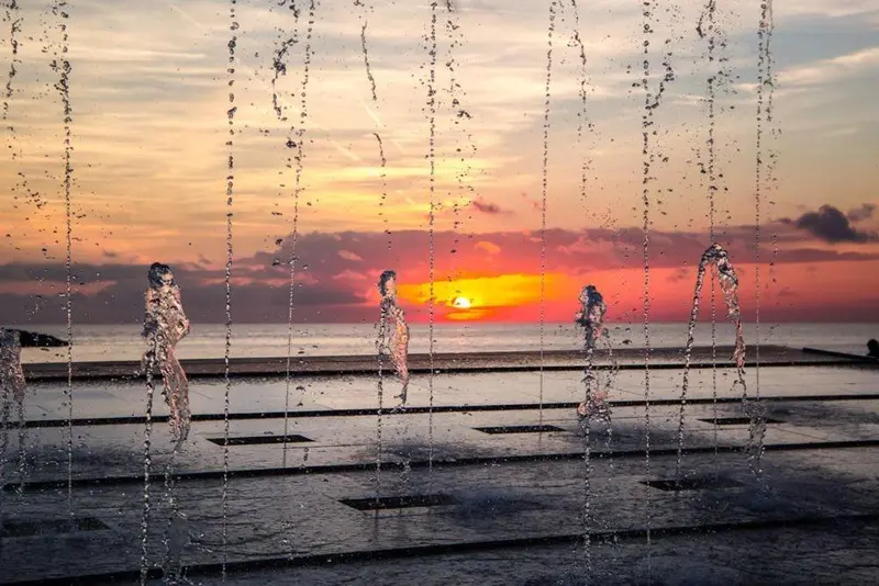 Jets d'eau illuminés par le soleil couchant sur une plage.
