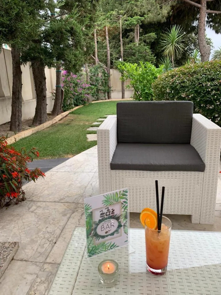 Une table basse avec un cocktail et un menu devant des fauteuils en osier sur une terrasse.
