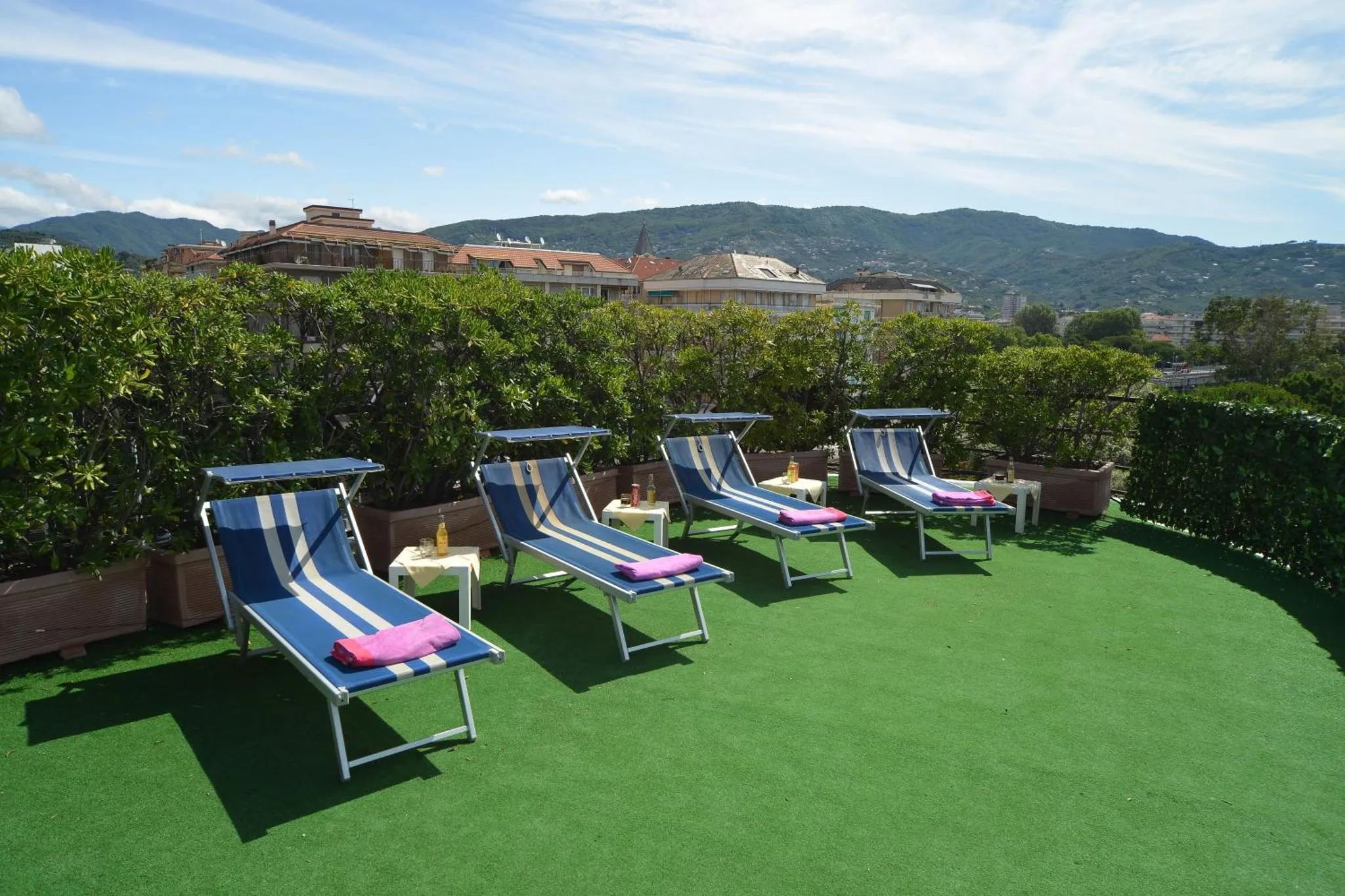 Transats bleus et roses sur une terrasse verdoyante avec vue sur la ville et les montagnes.