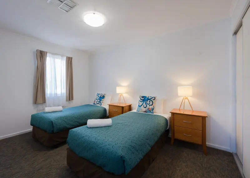 Chambre lumineuse avec deux lits simples et des tables de chevet.