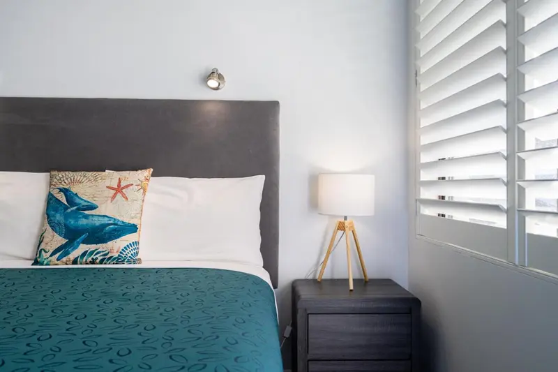 Un lit avec une couverture bleue et un oreiller décoré dans une chambre lumineuse.