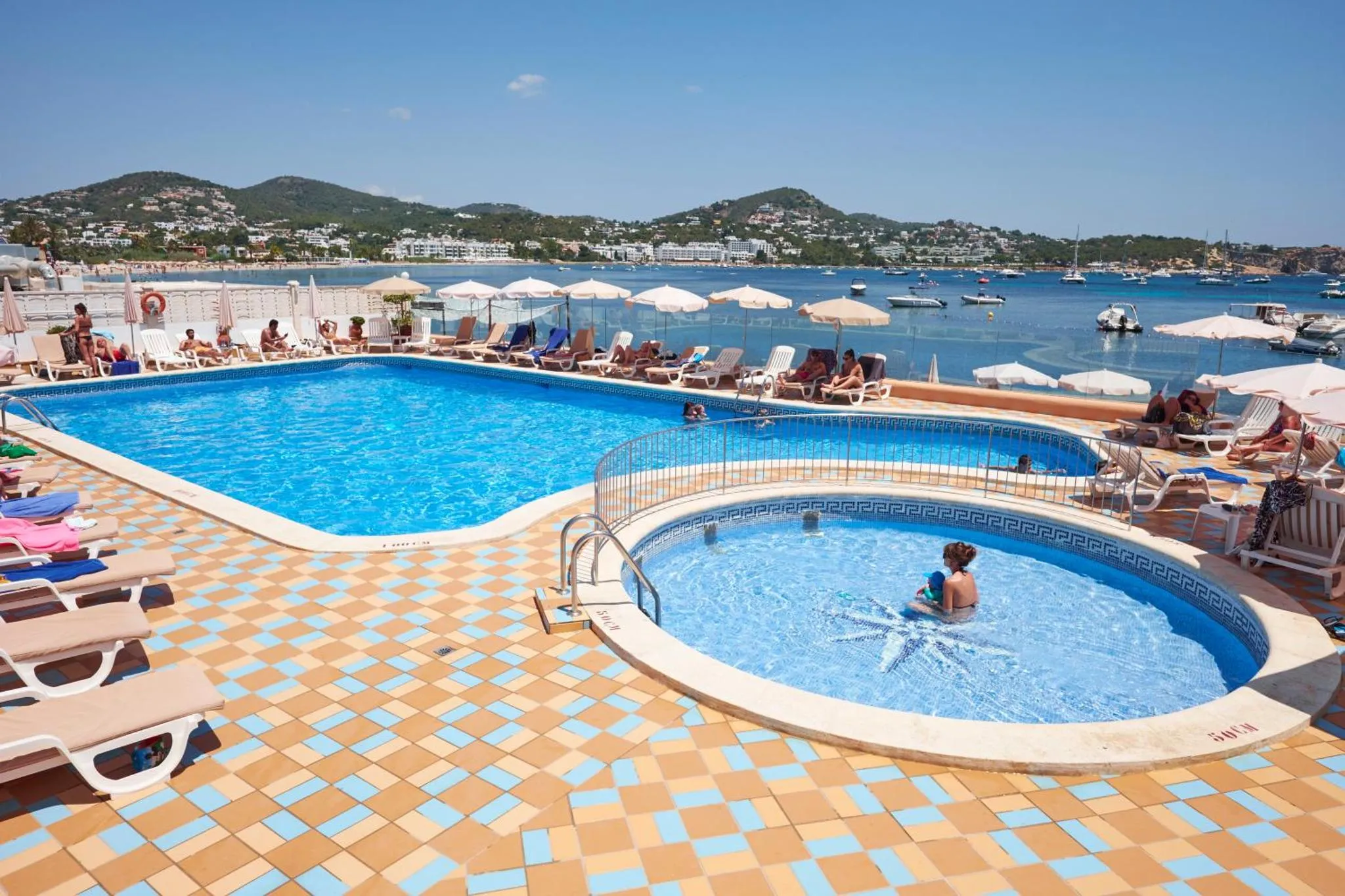 Une piscine avec des transats et des parasols offre une vue sur la mer et la côte.