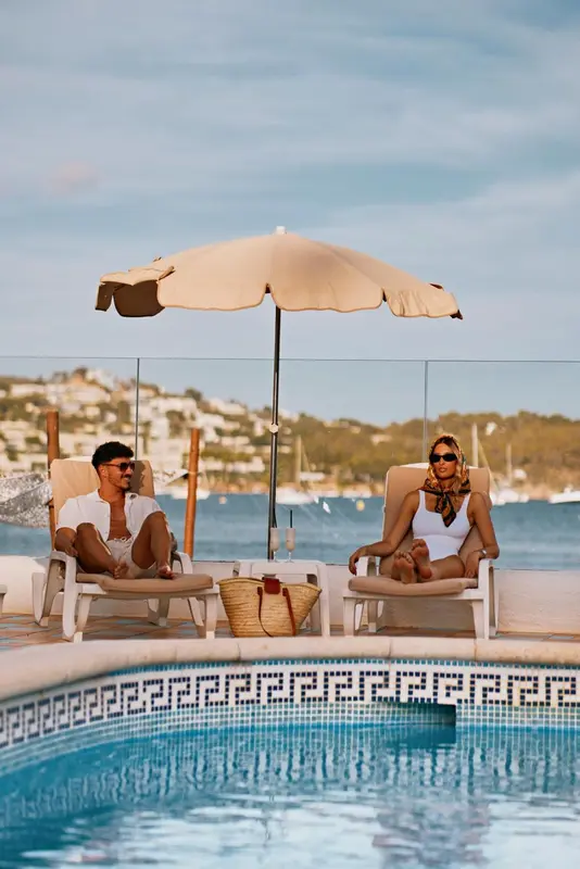 Deux personnes se relaxent sur des transats au bord d'une piscine avec vue sur la mer.