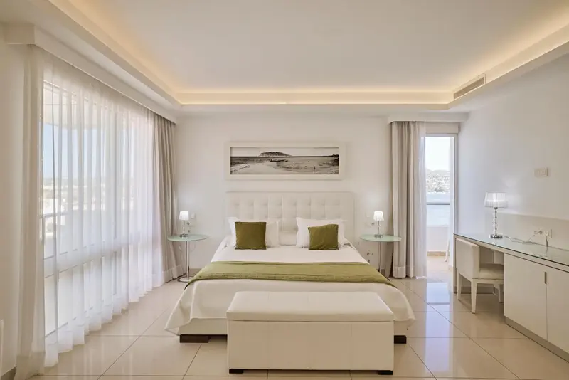 Chambre lumineuse avec un grand lit et un bureau.