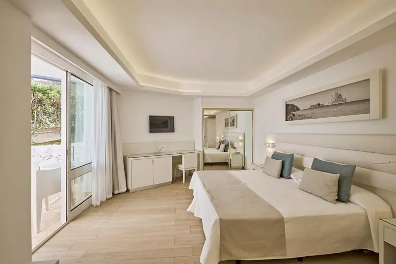 Chambre lumineuse avec un grand lit et un bureau près d'une baie vitrée.