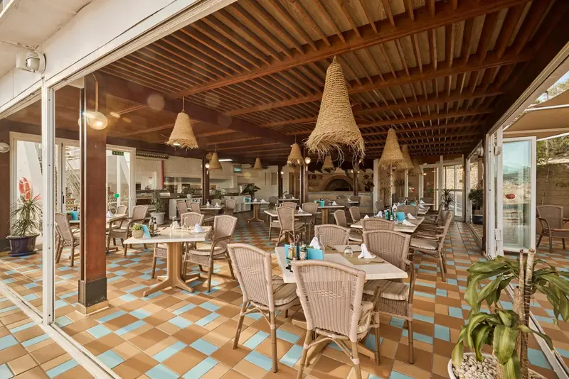 Une salle à manger lumineuse avec des tables dressées et des luminaires en osier.