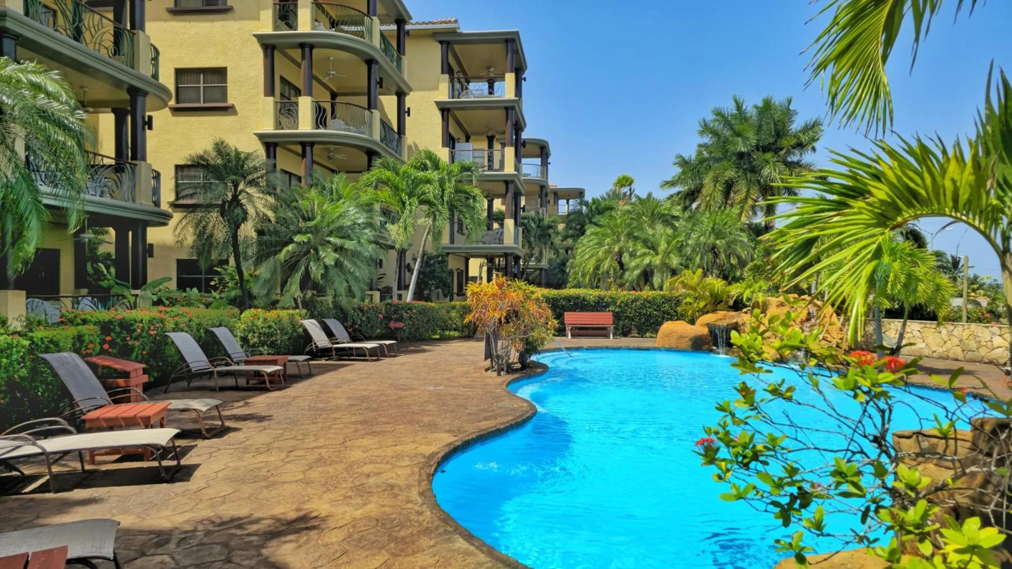 Piscine turquoise bordée de transats dans un jardin tropical luxuriant.