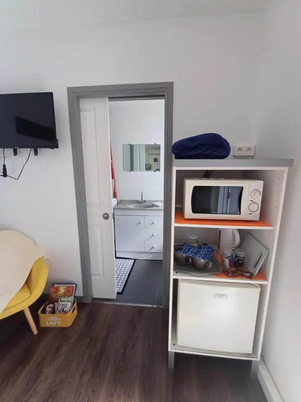 Une kitchenette avec un micro-ondes et un évier est visible dans un intérieur clair.