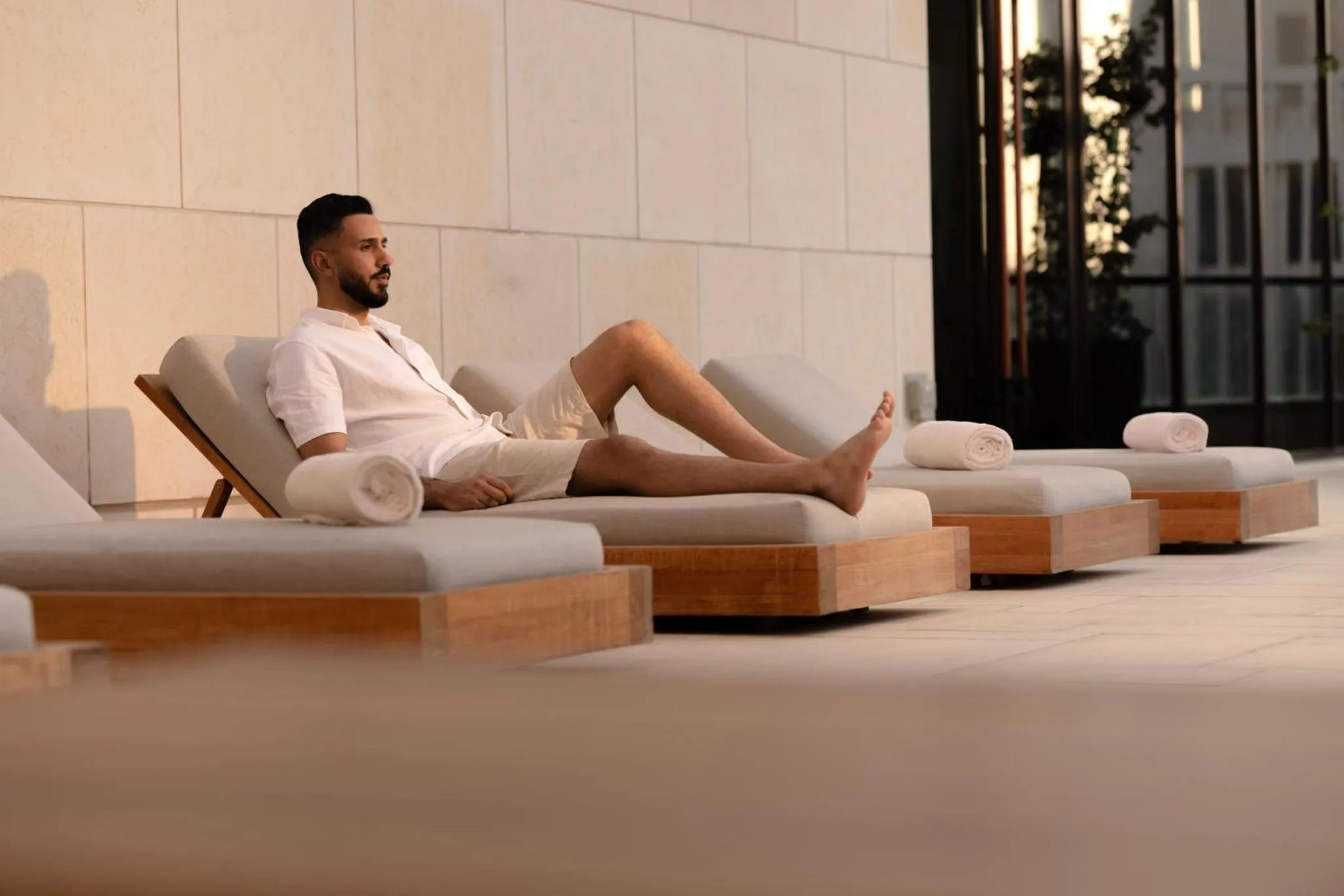 Un homme se repose sur des transats au bord d'une piscine.