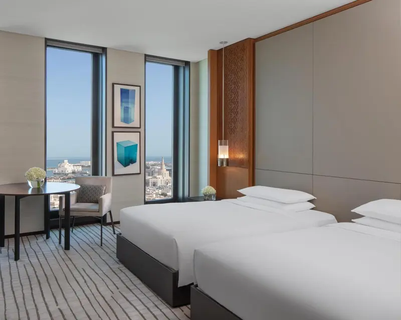 Une chambre moderne avec un grand lit et un coin salon donnant sur une vue urbaine.