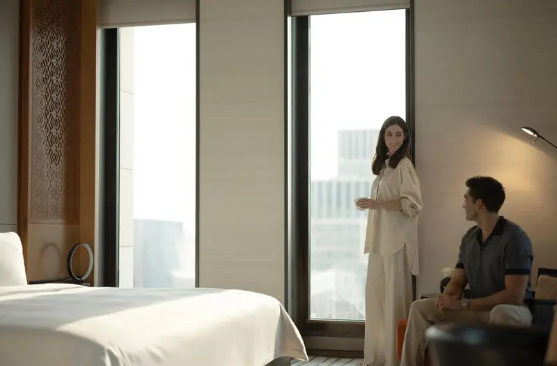 Un couple se tient dans une chambre d'hôtel lumineuse avec vue sur la ville.