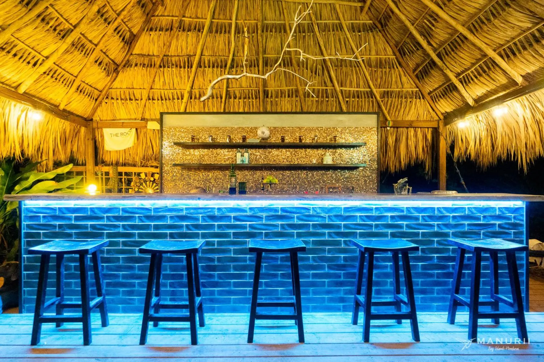 Un bar éclairé avec un comptoir bleu et des tabourets en bois.