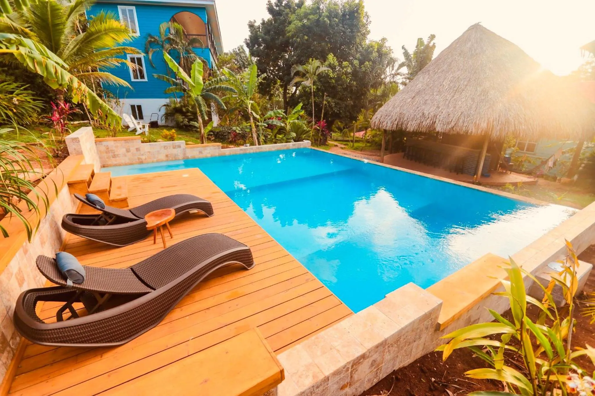 Transats noirs disposés autour d'une piscine turquoise bordée d'une terrasse en bois.