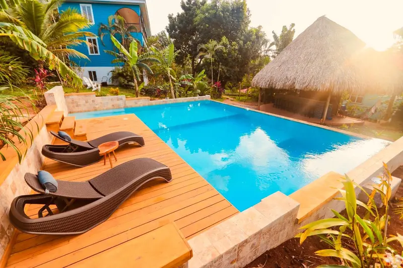 Transats noirs disposés autour d'une piscine turquoise bordée d'une terrasse en bois.