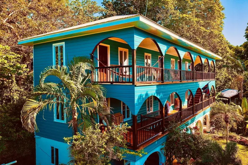 Bâtiment bleu turquoise à deux étages avec des balcons en bois et une végétation luxuriante.