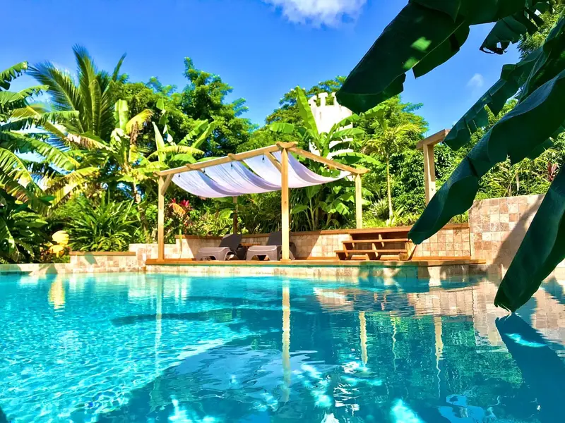 Une piscine turquoise bordée d'une terrasse en bois et de végétation luxuriante.