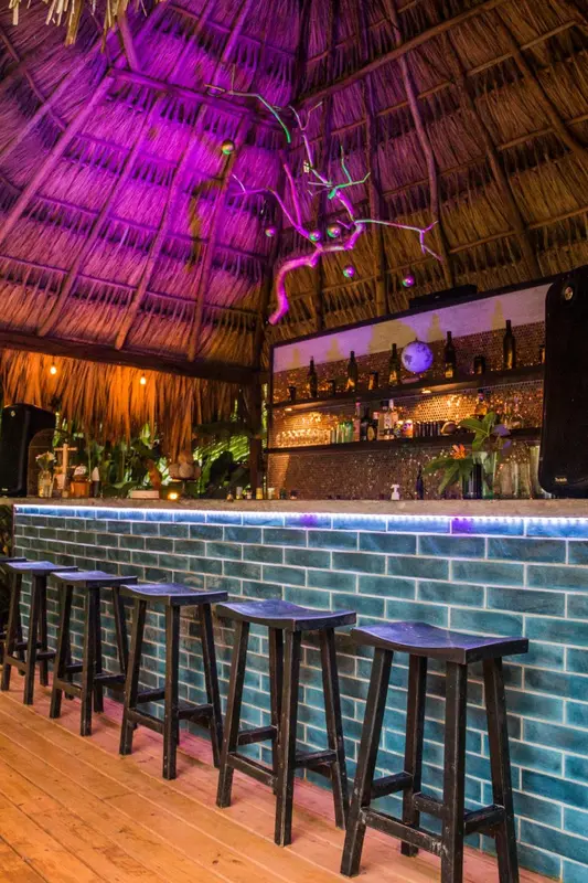 Un comptoir de bar illuminé avec des tabourets hauts et des bouteilles exposées.