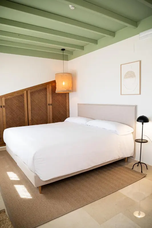 Une chambre lumineuse avec un lit recouvert de draps blancs et une décoration minimaliste.