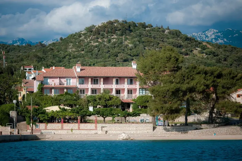 Bâtiment rose avec des balcons donnant sur la mer et les montagnes.