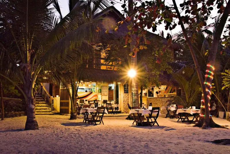 Terrasse de restaurant éclairée au crépuscule avec tables et chaises sur le sable.