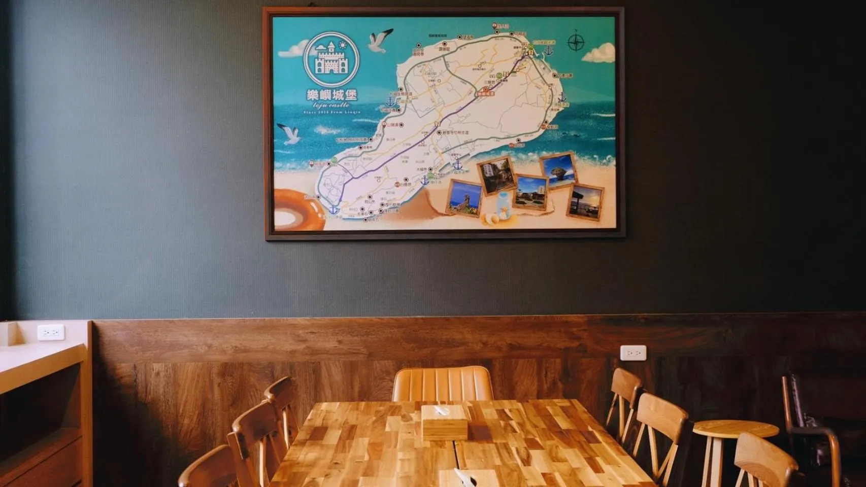 Table en bois et chaises dans une salle aux murs sombres, avec une grande carte décorative au mur.