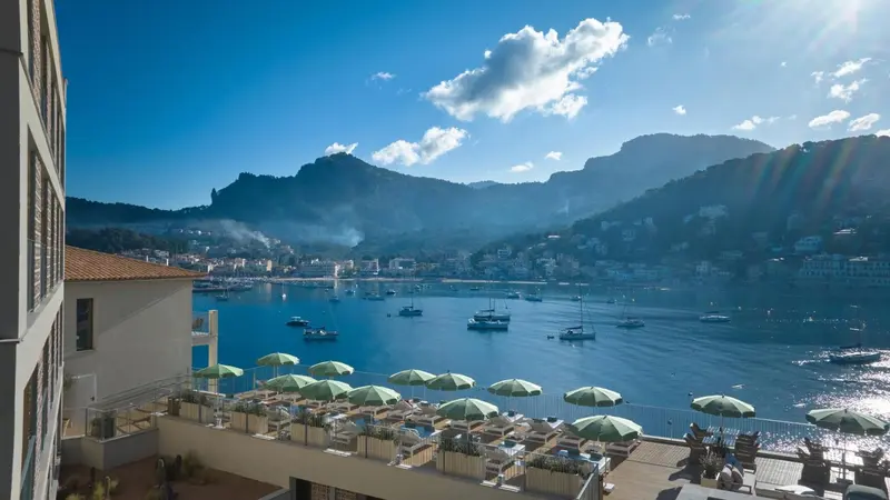 Vue d'une baie ensoleillée avec des bateaux et des montagnes en arrière-plan.