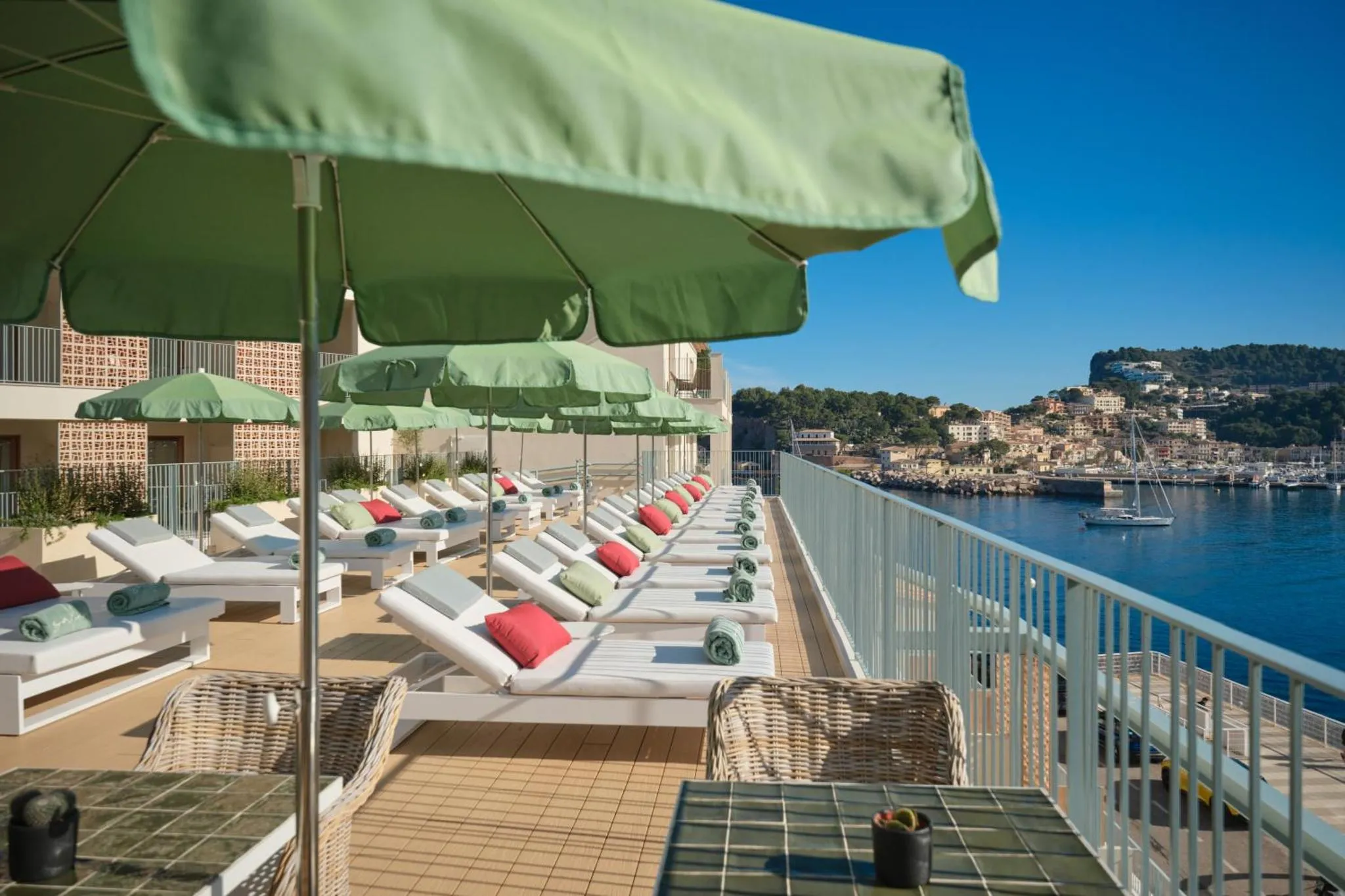 Transats verts et rouges alignés sur une terrasse ensoleillée avec vue sur la mer.