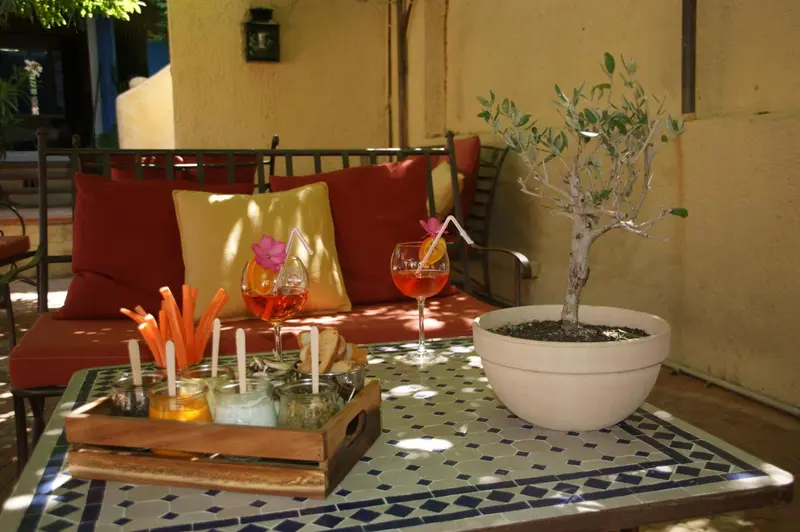 Une table basse colorée avec des boissons et des collations est placée devant un banc en fer forgé.