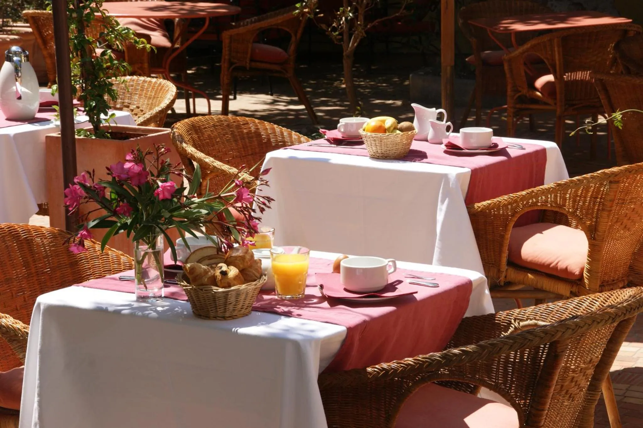Tables de petit-déjeuner ensoleillées sur une terrasse ombragée.