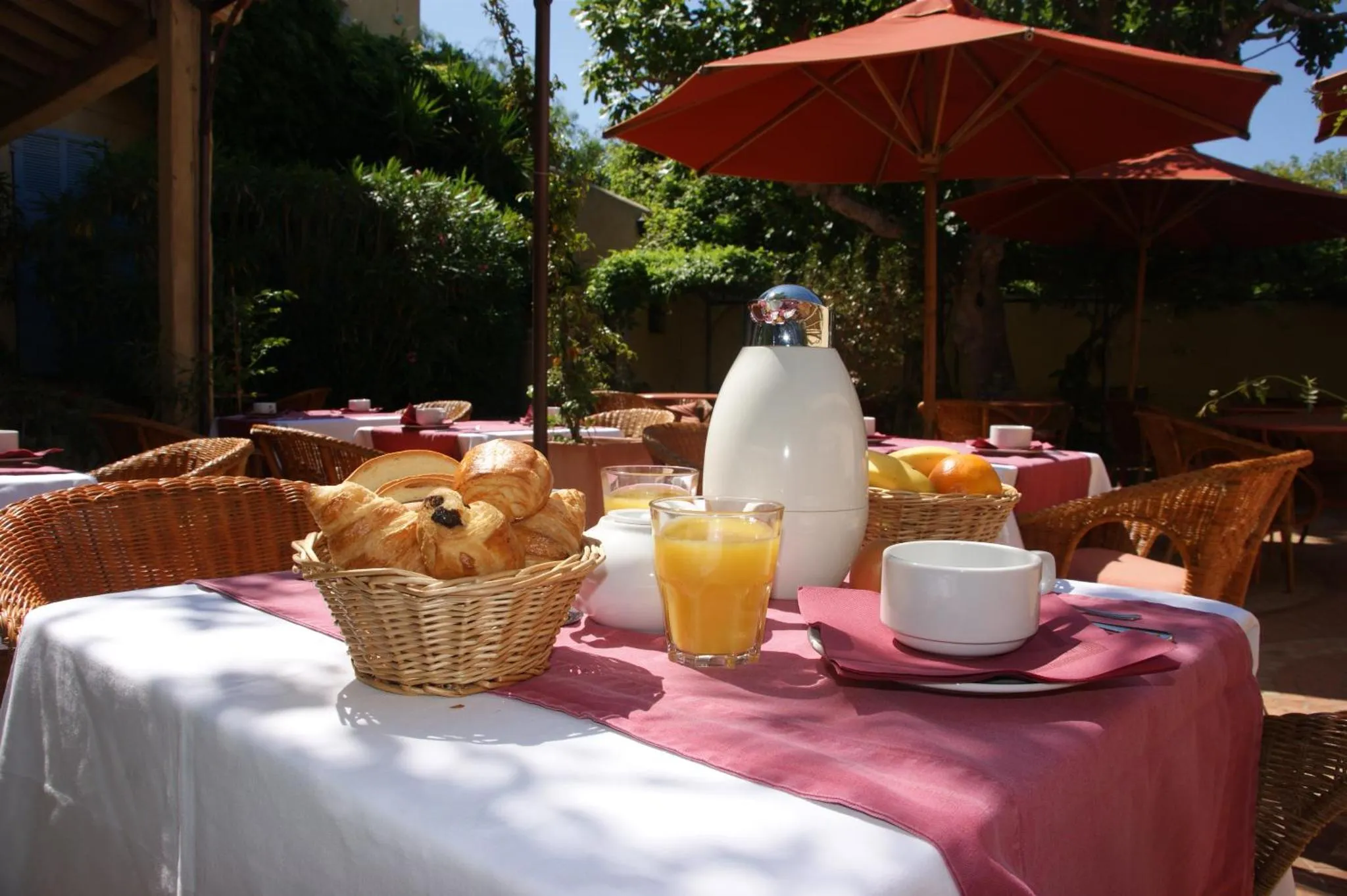 Une table est dressée avec des viennoiseries et des boissons sur une terrasse ombragée.