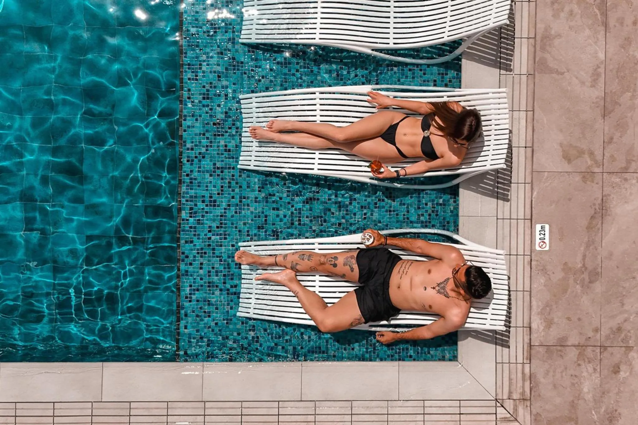 Deux personnes se relaxent sur des transats au bord d'une piscine turquoise.
