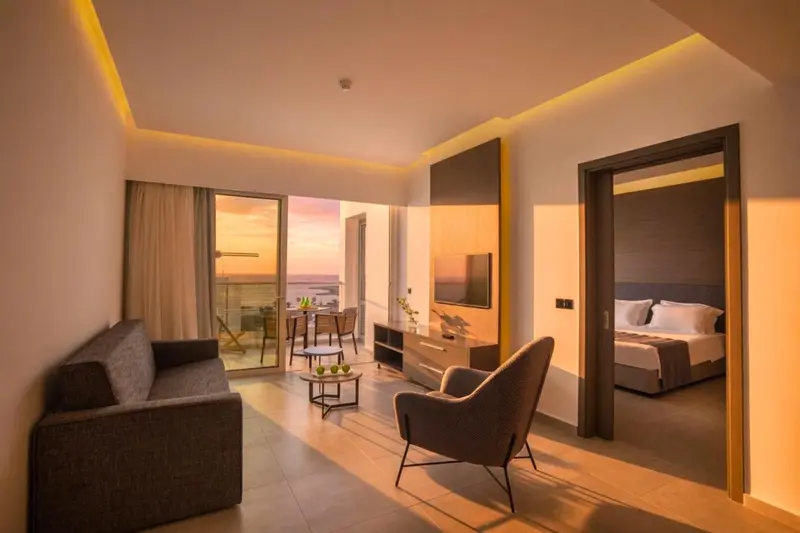 Espace de vie lumineux avec canapé, fauteuil et vue sur le coucher de soleil.