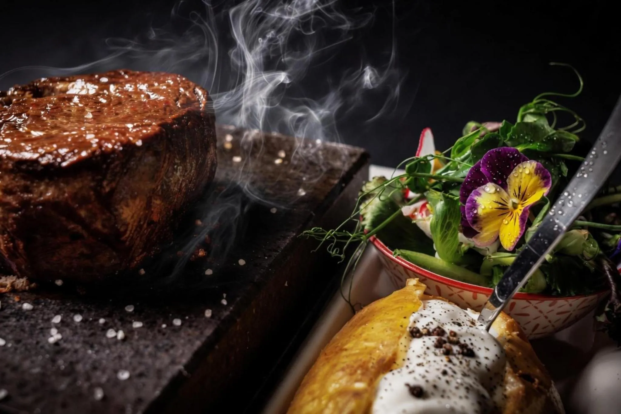 Un plat de viande grillée est présenté avec une salade et un accompagnement.