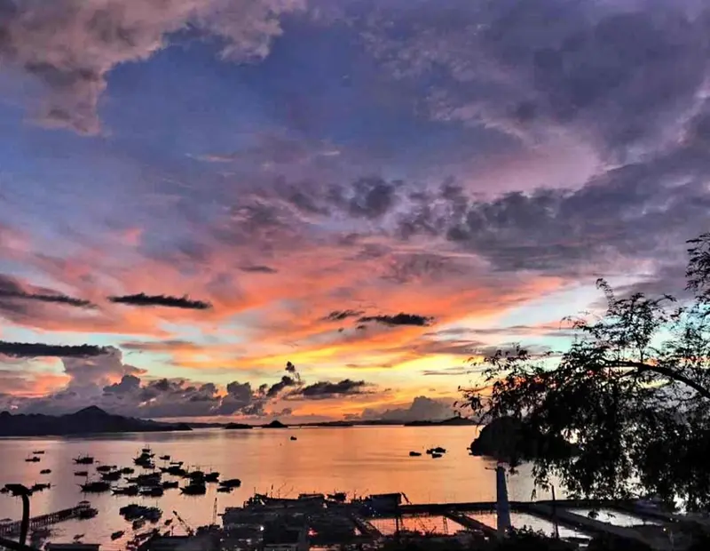 Ciel flamboyant au coucher du soleil sur une mer calme et des embarcations.