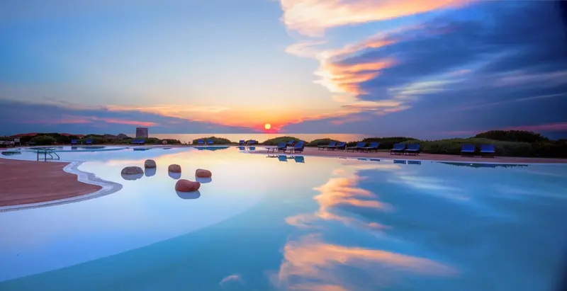 Une piscine reflète le ciel crépusculaire et les palmiers environnants.