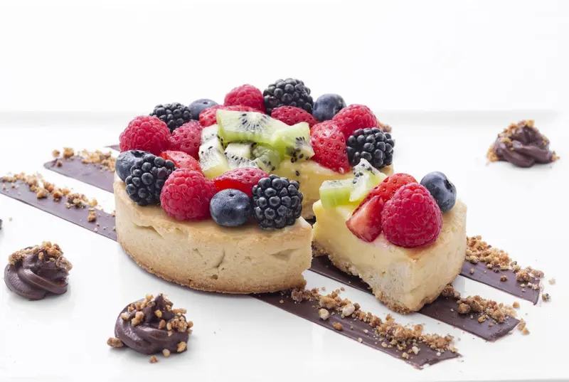 Une part de gâteau aux fruits frais est présentée sur une assiette blanche.