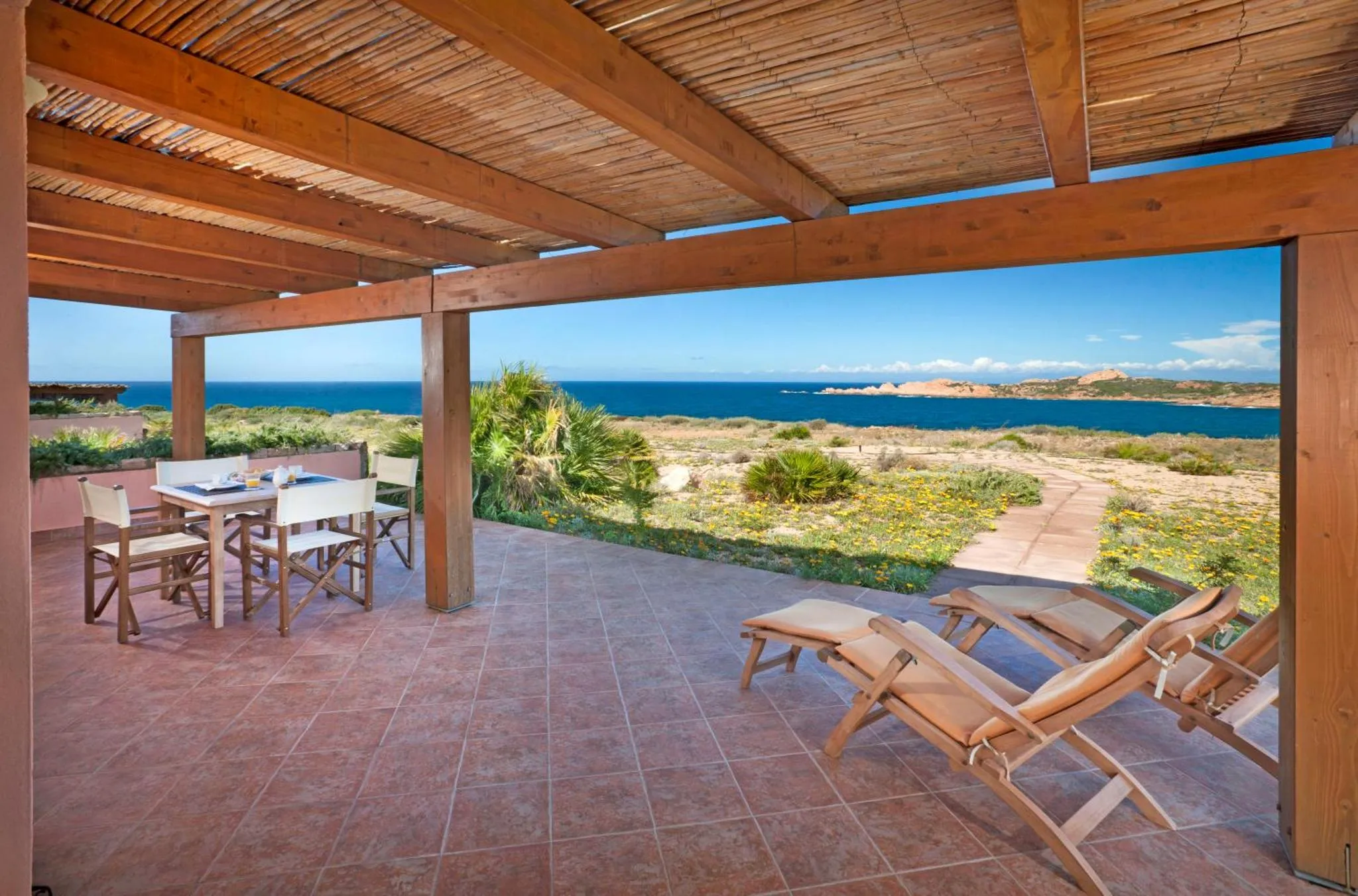 Terrasse ombragée avec mobilier de jardin et vue sur la mer.
