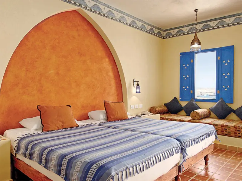 Une chambre lumineuse avec un lit double et une banquette décorative.