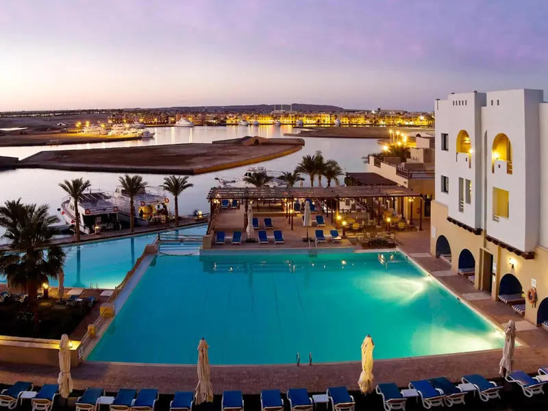 Vue aérienne d'une piscine d'hôtel au crépuscule avec un port en arrière-plan.