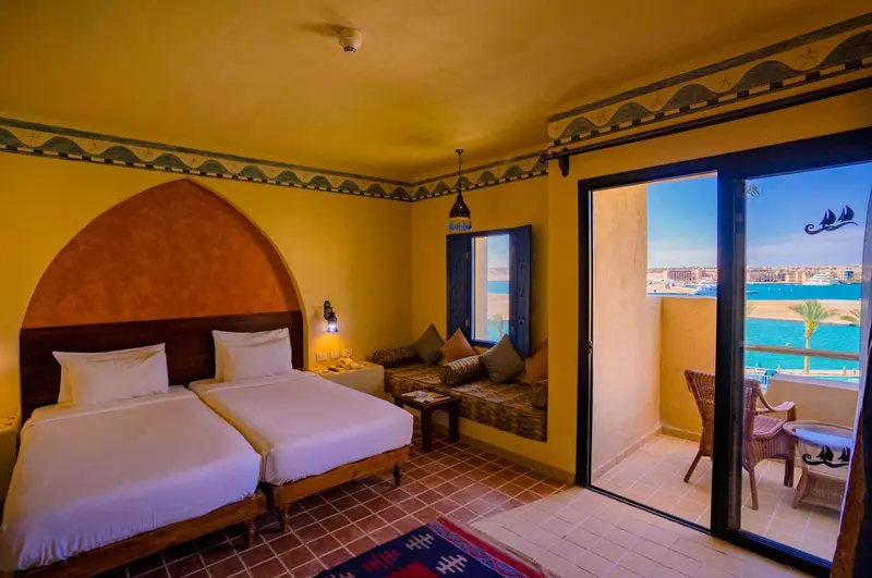 Chambre lumineuse avec deux lits simples et balcon donnant sur la mer.