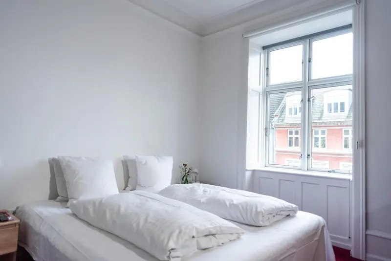 Une chambre lumineuse avec un lit simple et une vue sur des bâtiments.