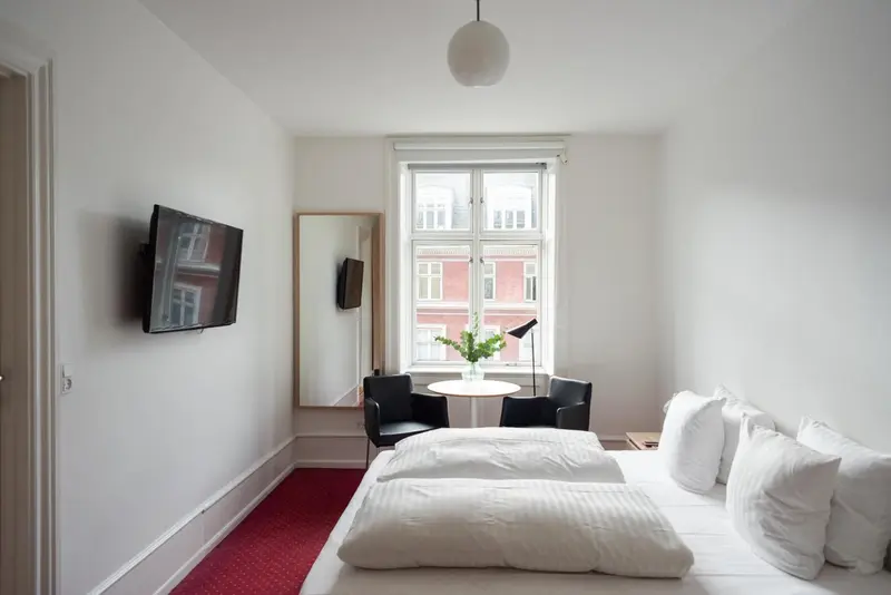 Une chambre lumineuse avec un lit, une fenêtre et un téléviseur mural.