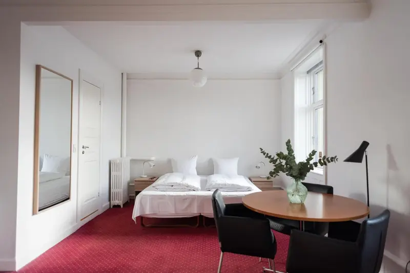 Une chambre lumineuse avec un lit, un miroir et une table ronde.