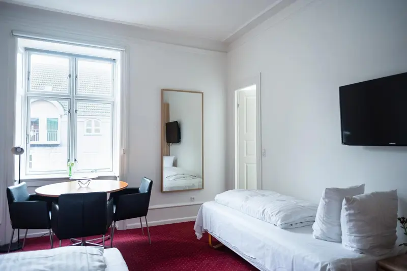 Une chambre lumineuse avec un lit simple, un coin repas et un grand miroir.