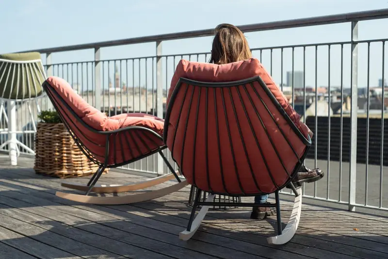 Deux fauteuils en osier rouge sur une terrasse en bois avec vue sur la ville.