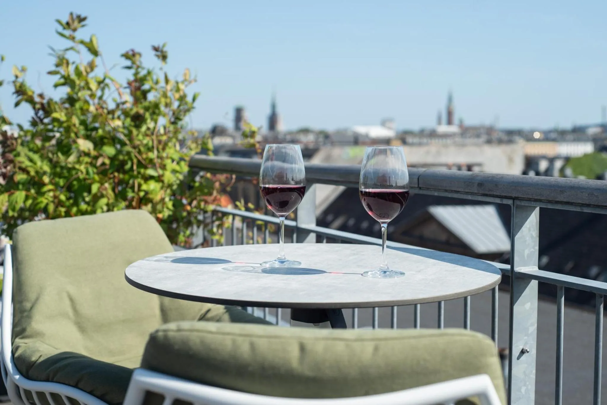 Deux verres de vin rouge sur une table ronde sur une terrasse avec vue sur la ville.