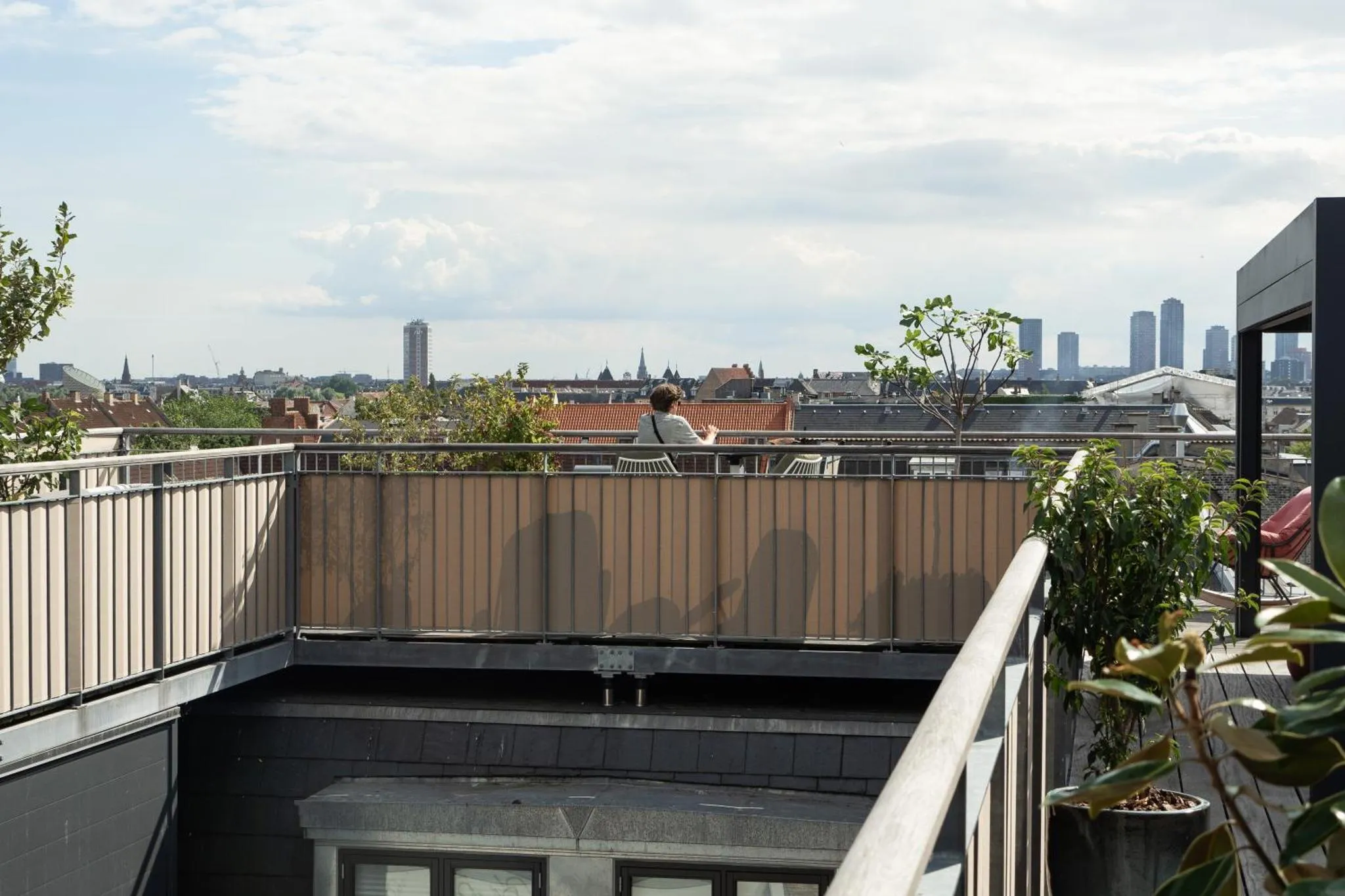 Une personne est assise à une table sur une terrasse avec vue sur la ville.