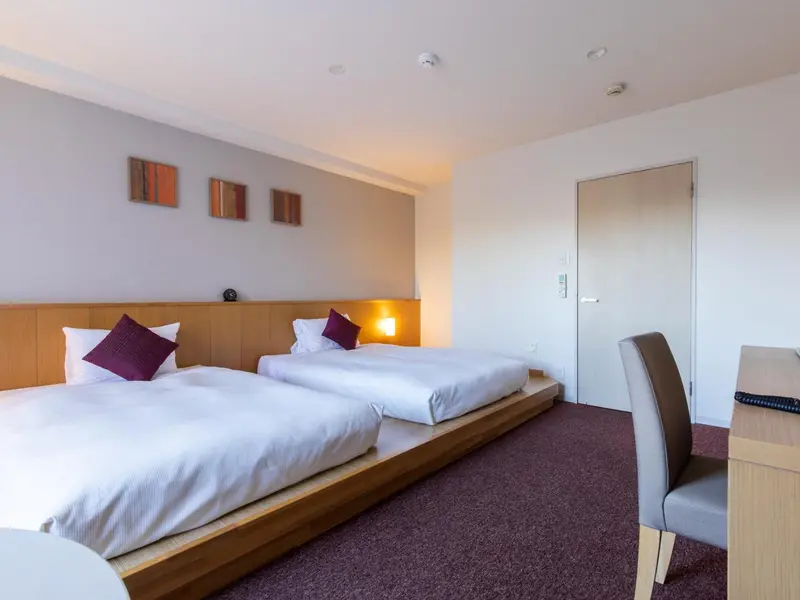 Une chambre avec deux lits simples et un espace bureau.